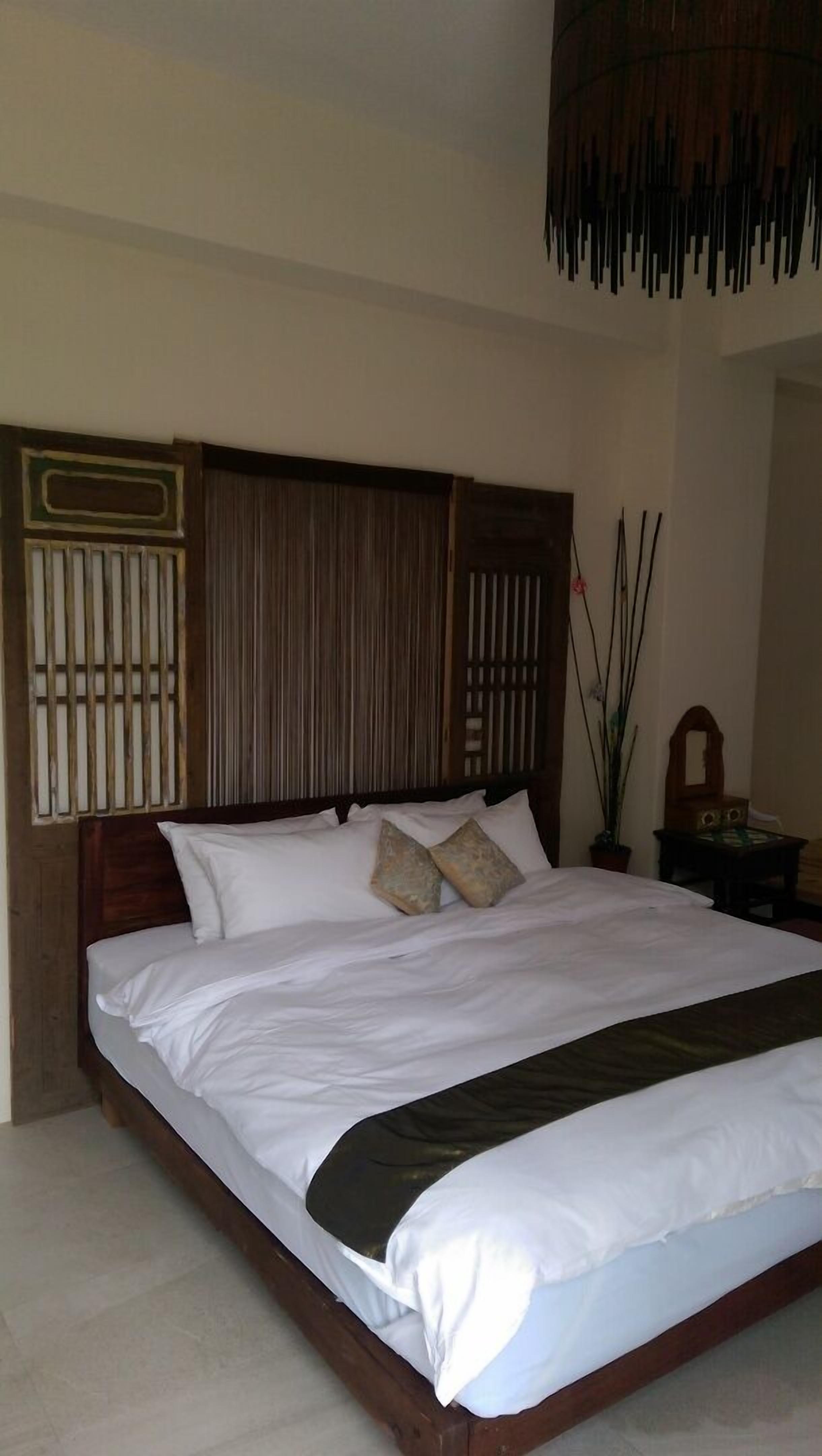 A neatly made bed with white linens and a dark headboard.