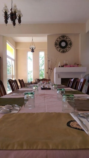 A dining room with a long table set for a meal, a chandelier, a fireplace, and a wall clock.