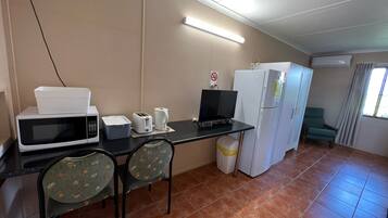 A compact kitchen with a microwave, toaster, and refrigerator, a small dining table with chairs, and a window with curtains.