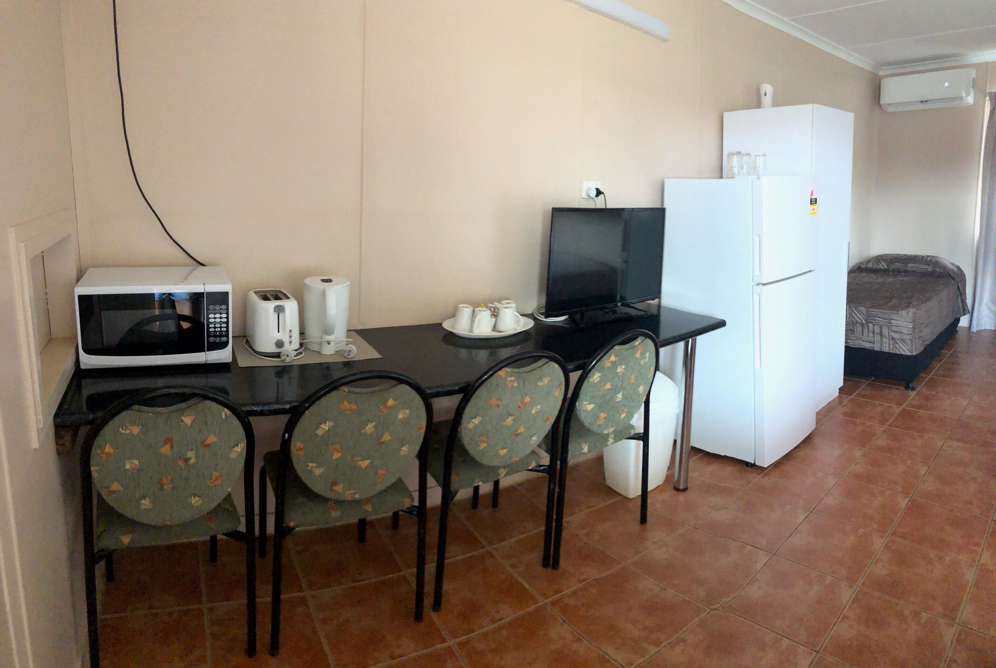 Cocina compacta con microondas, tostadora y refrigerador. Cuatro sillas rodean un pequeño comedor.