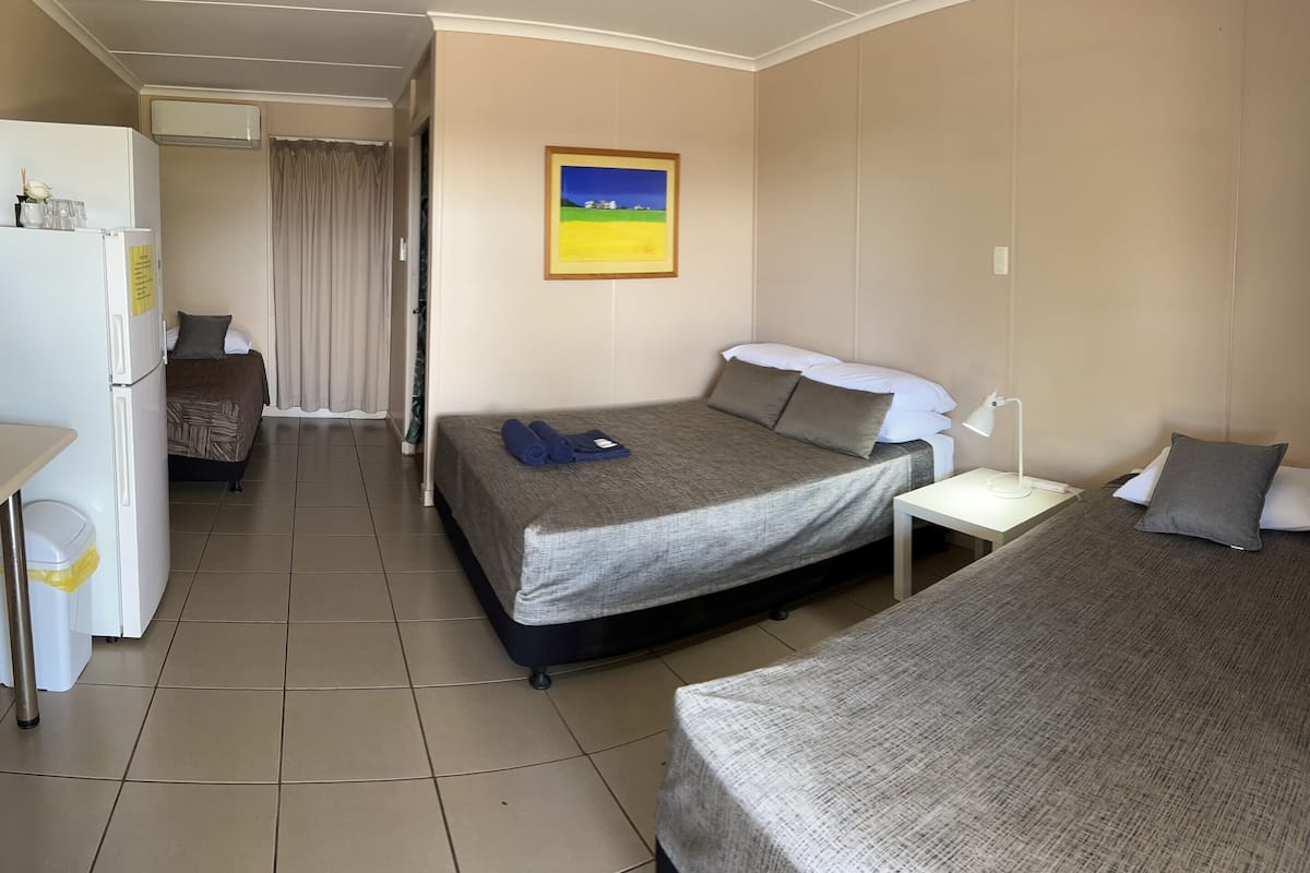 Habitación de hotel con dos camas individuales, una mesita, un refrigerador y un cuadro en la pared.