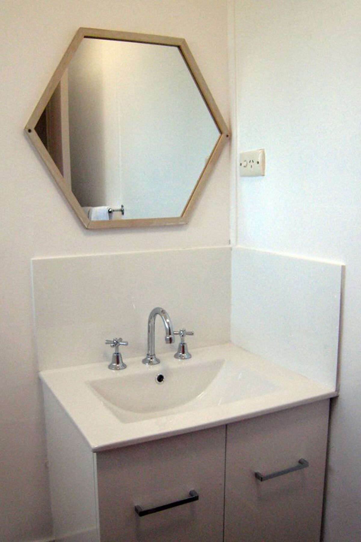 Un baño con un lavabo blanco, dos grifos y un espejo con marco de madera.