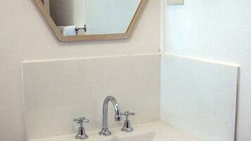 Un baño con un lavabo blanco, dos grifos y un espejo con marco de madera.