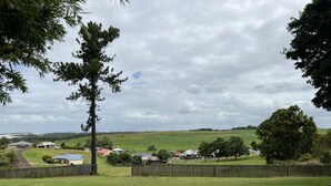 A rural landscape with houses, a fenced yard, and a cloudy sky. - Childers Budget Accommodation (Childers)