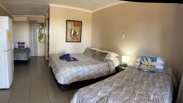 A hotel room with two beds, a small table with a lamp, a refrigerator, and a painting on the wall. - Childers Budget Accommodation (Childers)