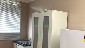 A kitchen with a white refrigerator, a built-in sink, and a cabinet with frosted glass doors. - Childers Budget Accommodation (Childers)