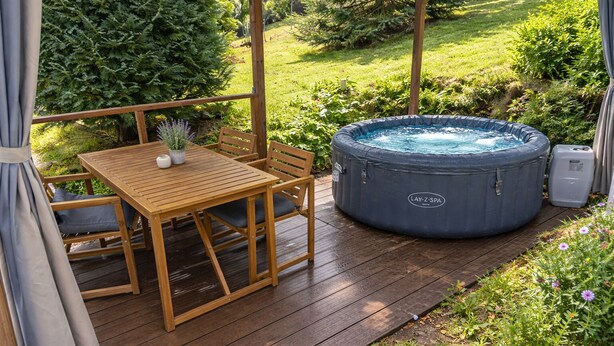 Una terraza de madera con un jacuzzi, una mesa y sillas.