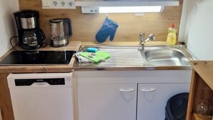 Una cocina compacta equipada con lavavajillas, estufa, pileta y una pequeña alacena con utensilios de cocina.