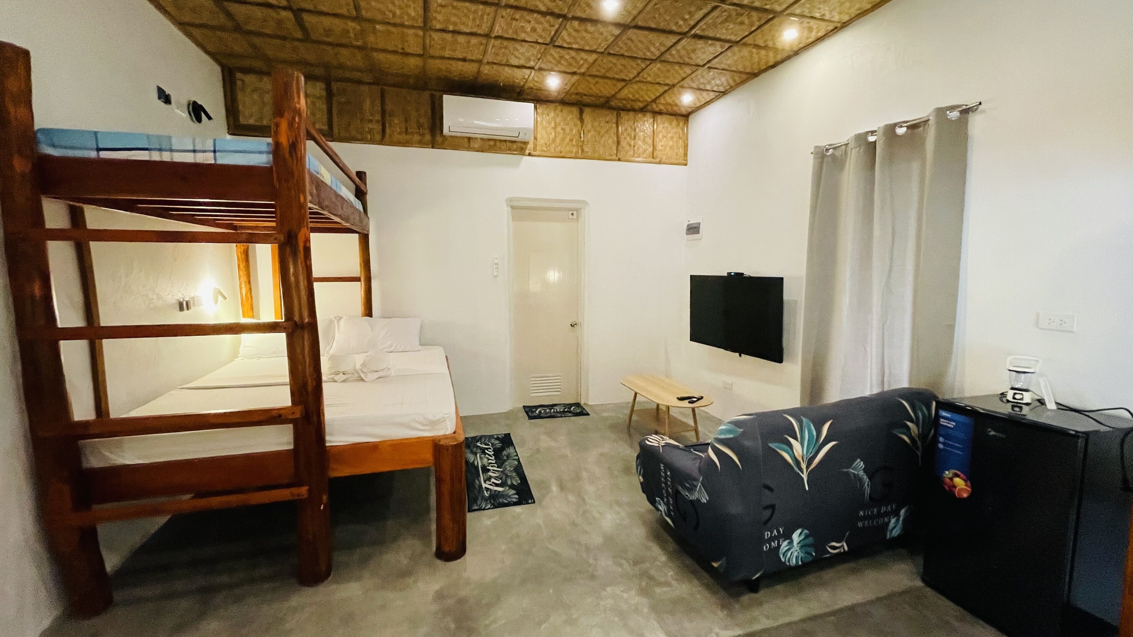 A bunk bed, a sofa, a TV, and a small table in a room with a wooden ceiling and white walls.