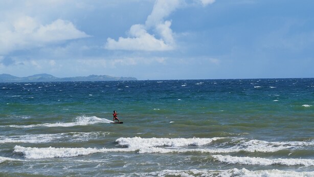 A person windsurfing with a kiteboard in the ocean, with a mountainous coastline in the background. - Footprints Beach Resort (San Andres)