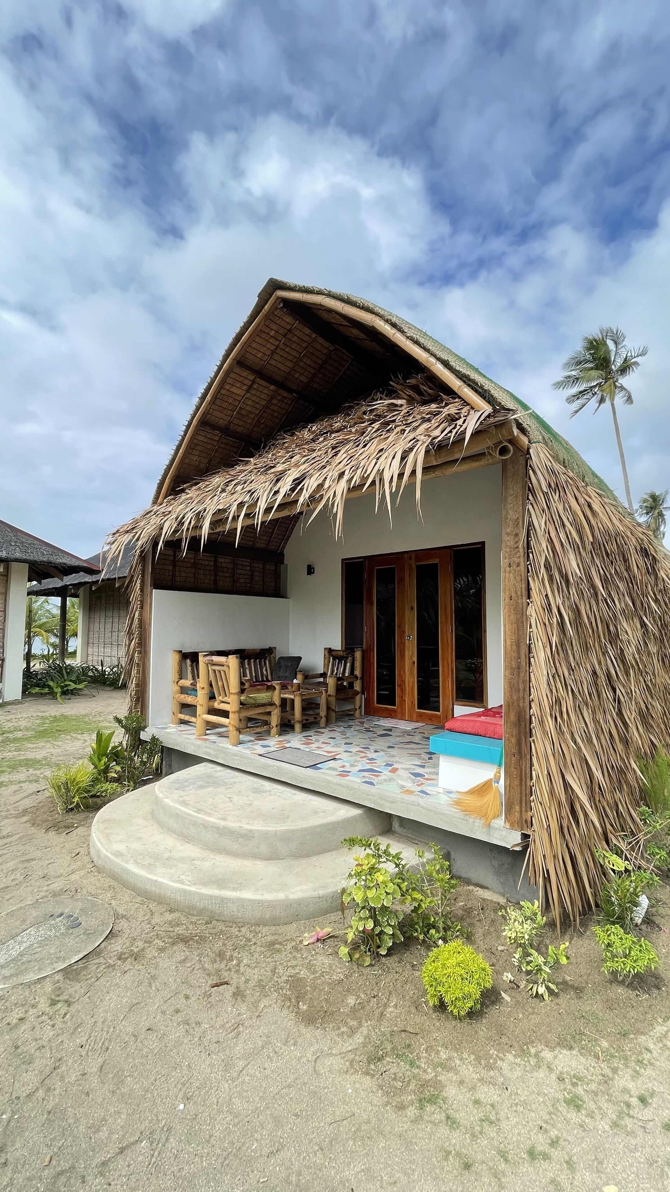 Ein Haus mit einem Strohdach, einer gefliesten Veranda und Holzmöbeln.