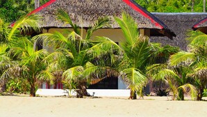 A beachfront property with a thatched roof structure, surrounded by palm trees and a sandy beach. - Footprints Beach Resort (San Andres)