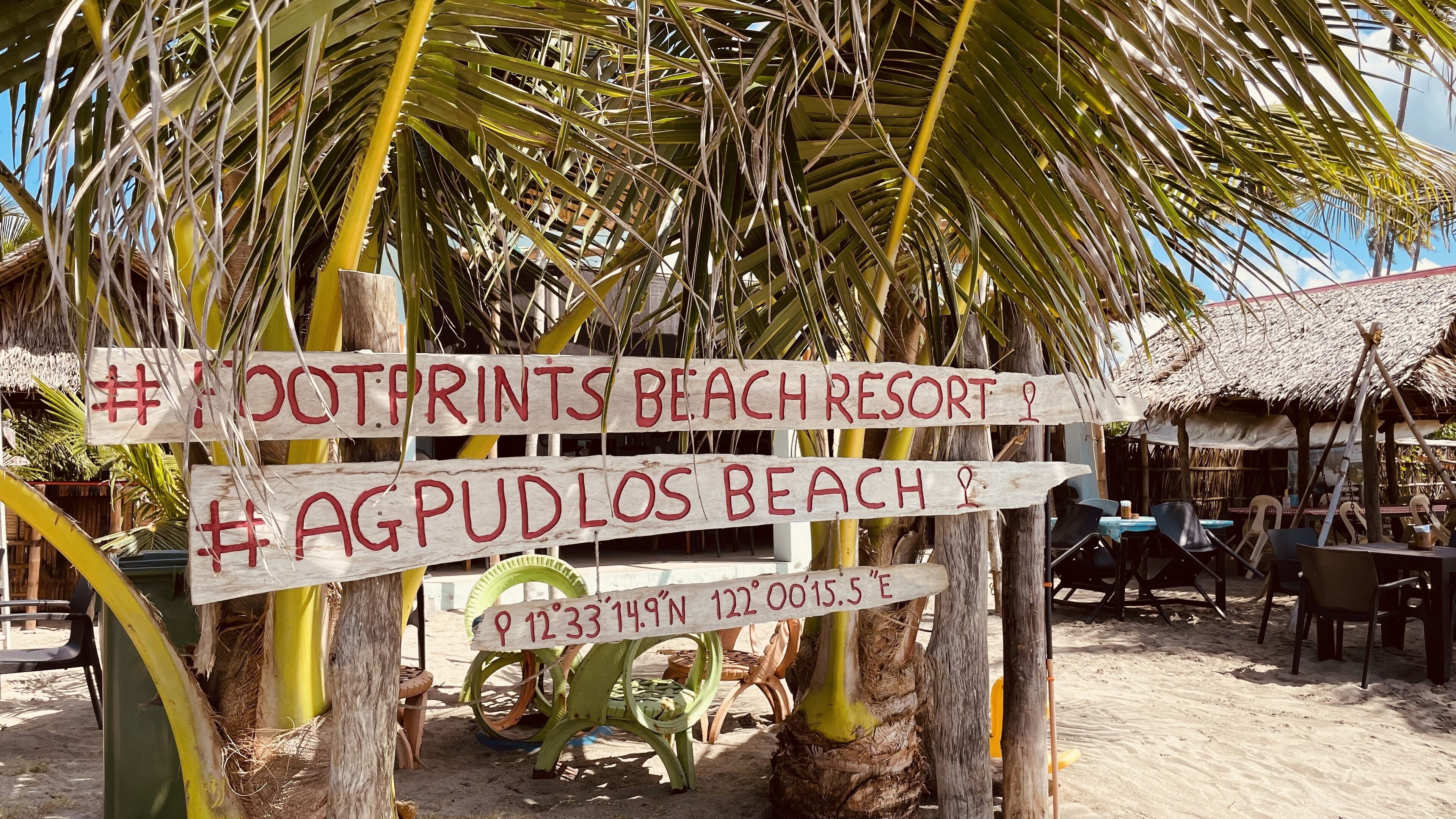 Wooden signs with red text indicating the location of #Footprints Beach Resort and #AgPudlos Beach.