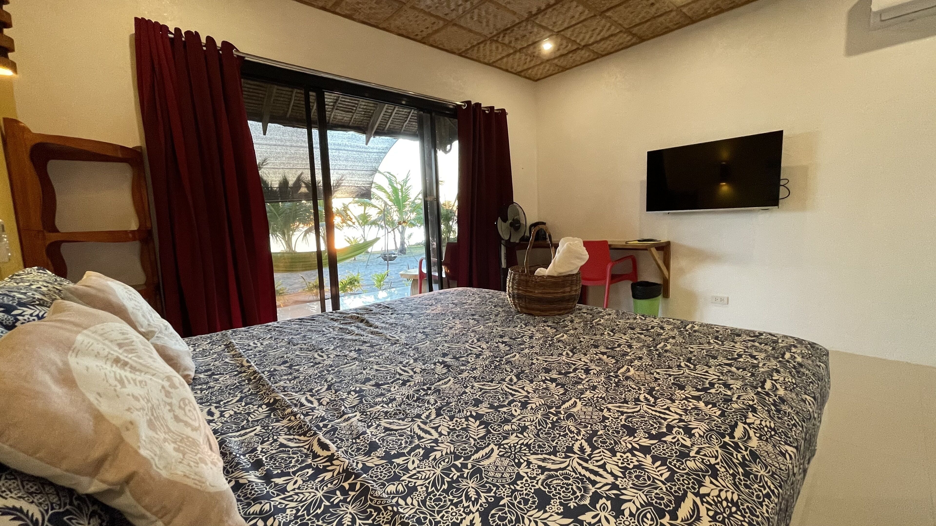 Camera da letto con un letto grande, una TV a parete e vista su una piscina e palme attraverso la finestra.
