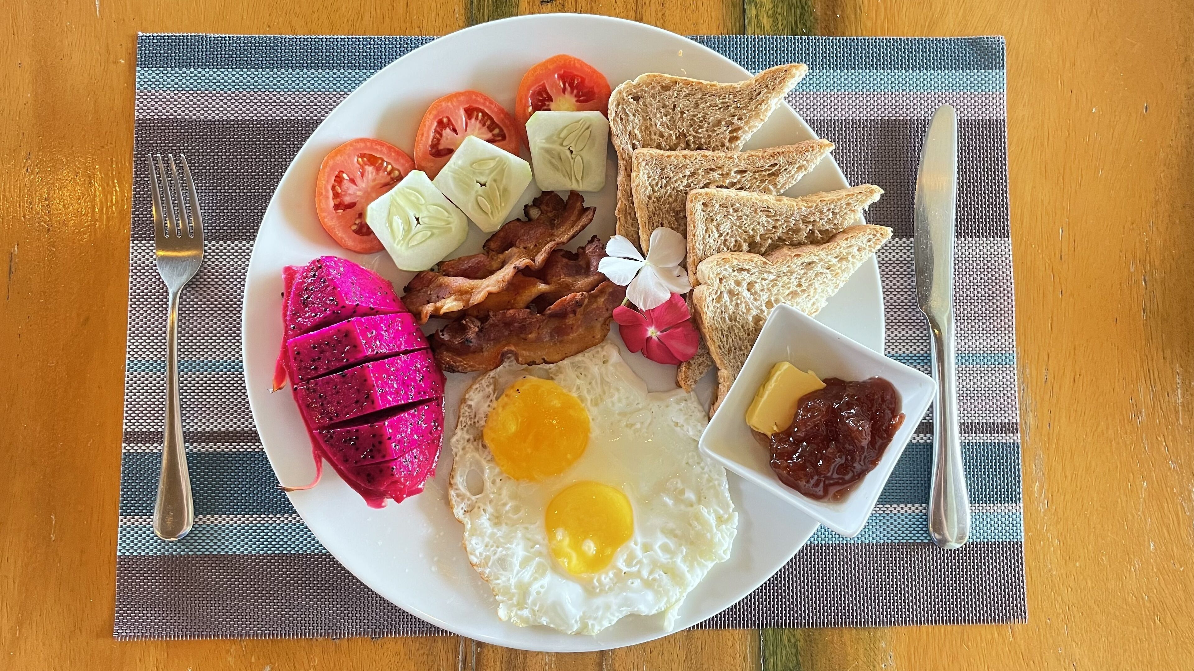 Une assiette de nourriture pour le petit-déjeuner comprenant des œufs, du bacon, des toasts, des tomates et une portion de confiture.