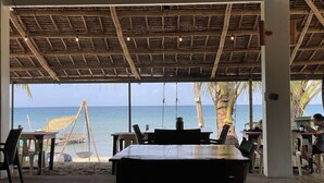 A beachside restaurant with a thatched roof, outdoor seating, and a view of the sea. - Footprints Beach Resort (San Andres)