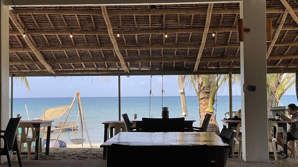 Un restaurante frente al mar con techo de paja, mesas al aire libre y vista al océano.
