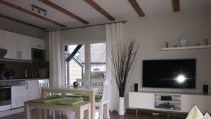 Un salon moderne comprenant un coin repas, une cuisine et un téléviseur fixé au mur.
