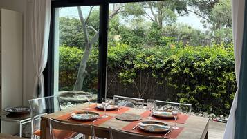 Un coin repas avec une table dressée pour six personnes, des chaises transparentes et une vue sur le jardin grâce à de grandes fenêtres.