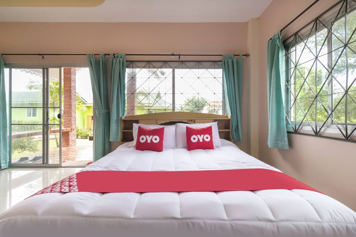 A neatly made bed with white bedding and two red pillows with the word "OYO" on them.