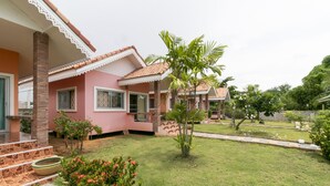 A pink house with a tiled roof, a small garden with a palm tree, and a paved area with a white fence. - OYO 949 Sansuk Resort Paknampran (Pranburi)