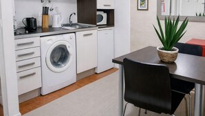 A compact kitchen with a washing machine, a dining table with chairs, and a potted plant.