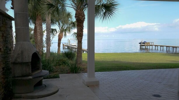 A patio area with a stone oven, palm trees, and a view of the sea and a pier. - Romantic Escape; Open Gulf View; Your Own Private Dock!  Elevator to master. (Crystal Beach)