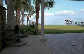 A patio area with a stone oven, palm trees, and a view of the sea and a pier. - Romantic Escape; Open Gulf View; Your Own Private Dock!  Elevator to master. (Crystal Beach)