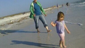 A sandy beach with a person and a child walking on the shore. - Romantic Escape; Open Gulf View; Your Own Private Dock!  Elevator to master. (Crystal Beach)