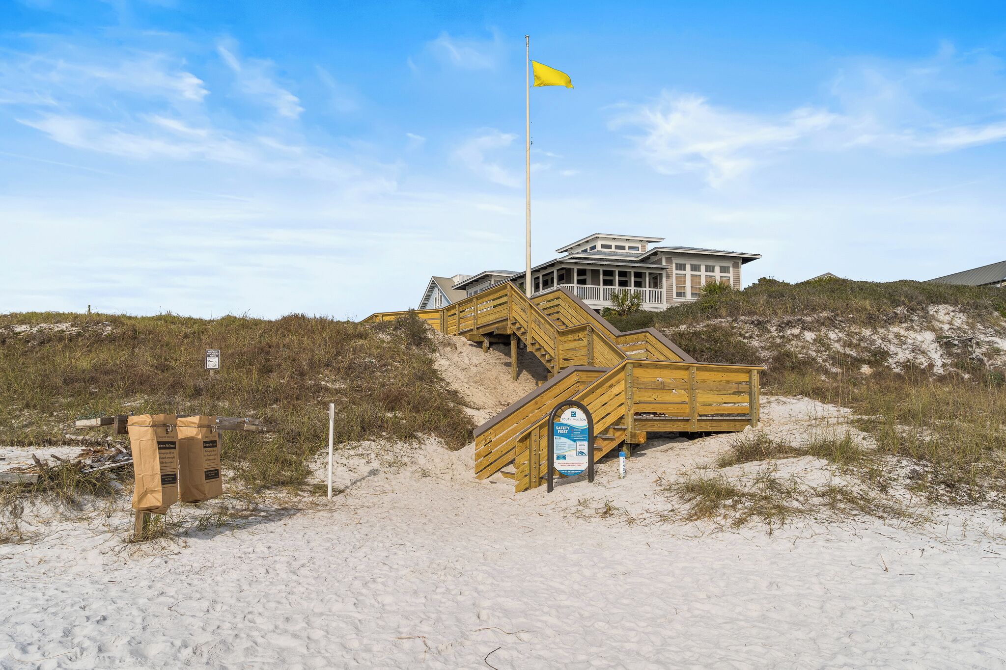 A sandy beach with a wooden staircase leading to a building, a flagpole, and a sign.