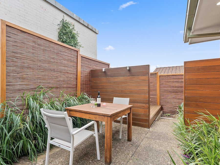 A patio with a table and chairs, surrounded by plants and a wooden fence.