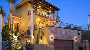 Une maison à deux étages avec un balcon, des palmiers et des cactus.