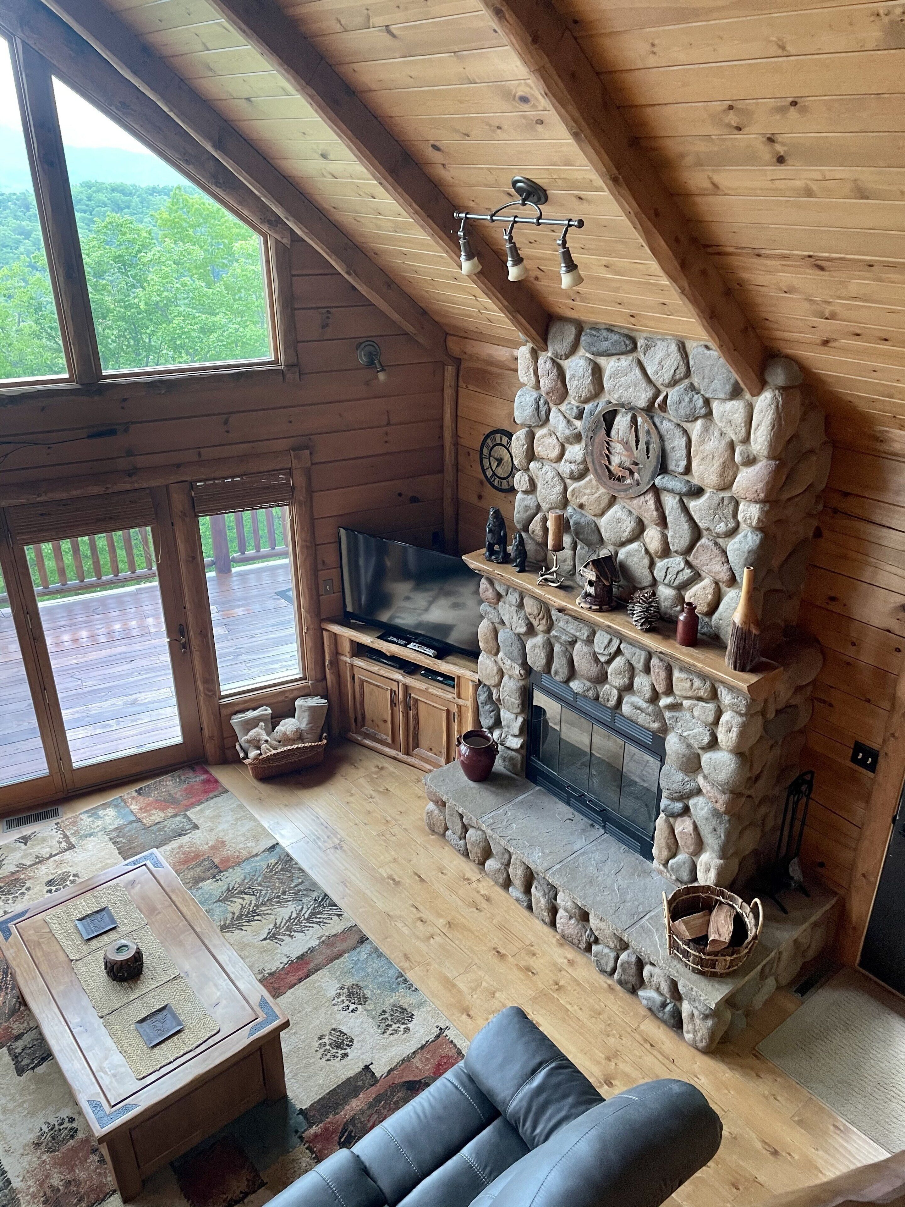 Interior acogedor de una cabaña con chimenea de piedra, paredes de madera y un ventanal con vistas a una terraza.