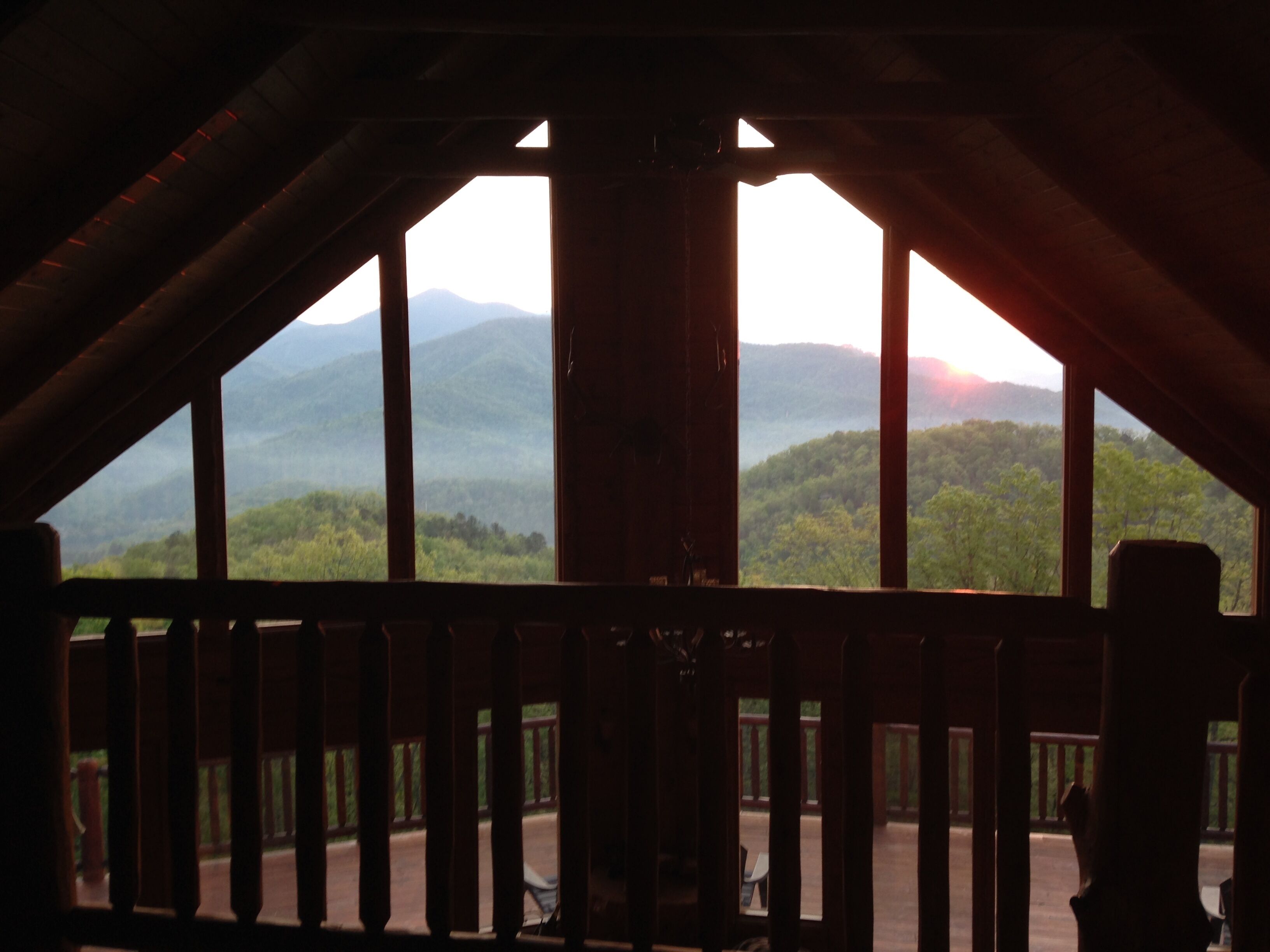 A view from a balcony with a wooden railing, overlooking a mountainous landscape.