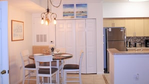 Una cocina con comedor, que incluye una araña, armarios blancos, un refrigerador y un salpicadero de azulejos.