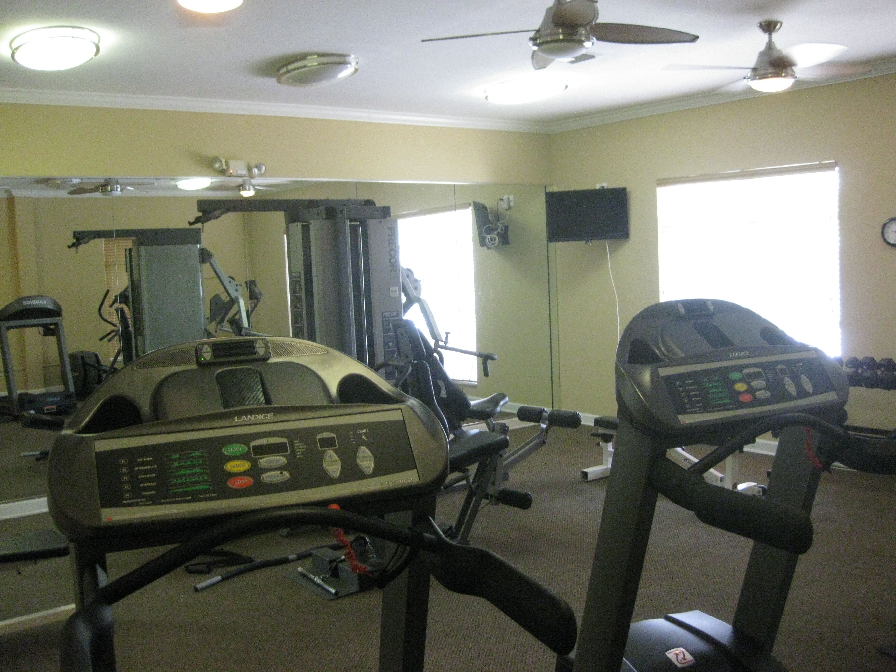 Un gimnasio con equipo de ejercicio, cinta de correr y un espejo grande.