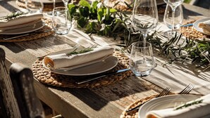 Ein Holztisch, gedeckt für eine Mahlzeit, mit gewobenen Unterlagen, klaren Gläsern und ordentlich gefalteten weißen Servietten.