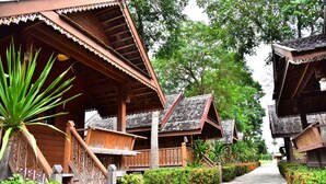 A pathway leading to traditional wooden buildings with intricate railings and a lush green environment. - Little Home Beach (Kui Buri)