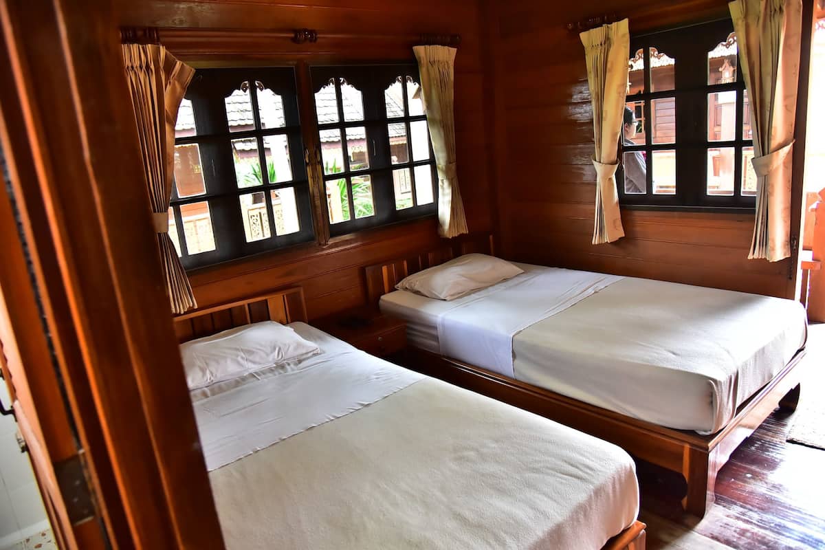 Habitación de cabaña de madera con dos camas, una ventana con cortinas y vistas al verde exterior.