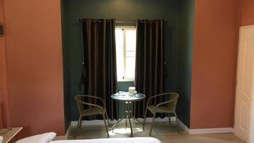A room with a bed, a small round table with two chairs, a window with curtains, and a door.
