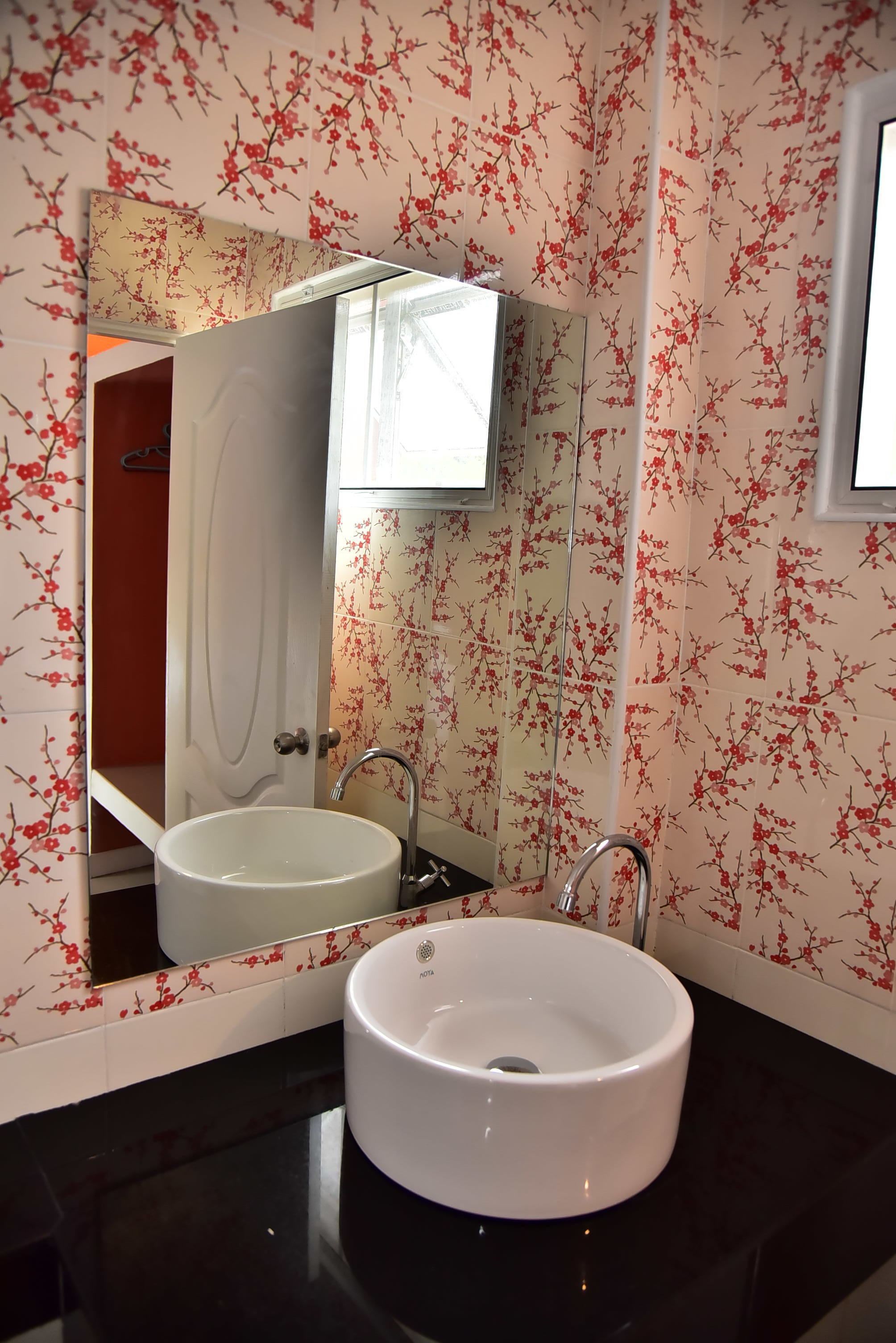Un baño con lavamanos blanco, un espejo y papel tapiz floral rojo.