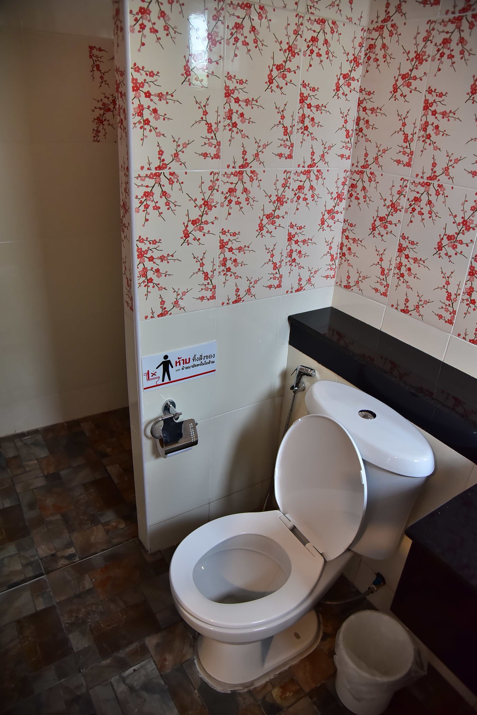 Un baño con inodoro, lavamanos y ducha. Las paredes tienen un estampado floral.