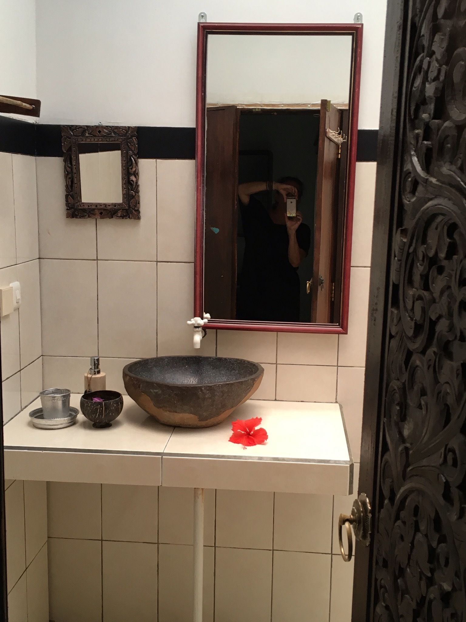 Un baño con un espejo grande, un lavabo de piedra, un cuenco pequeño y una flor roja sobre el mostrador.