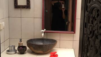 Un baño con un espejo grande, un lavabo de piedra, un cuenco pequeño y una flor roja sobre el mostrador.