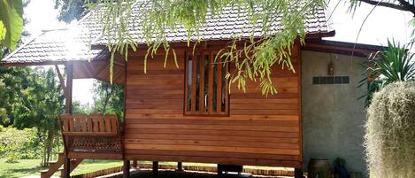 A wooden cabin with a tiled roof, a bench outside, and a garden path leading to it.