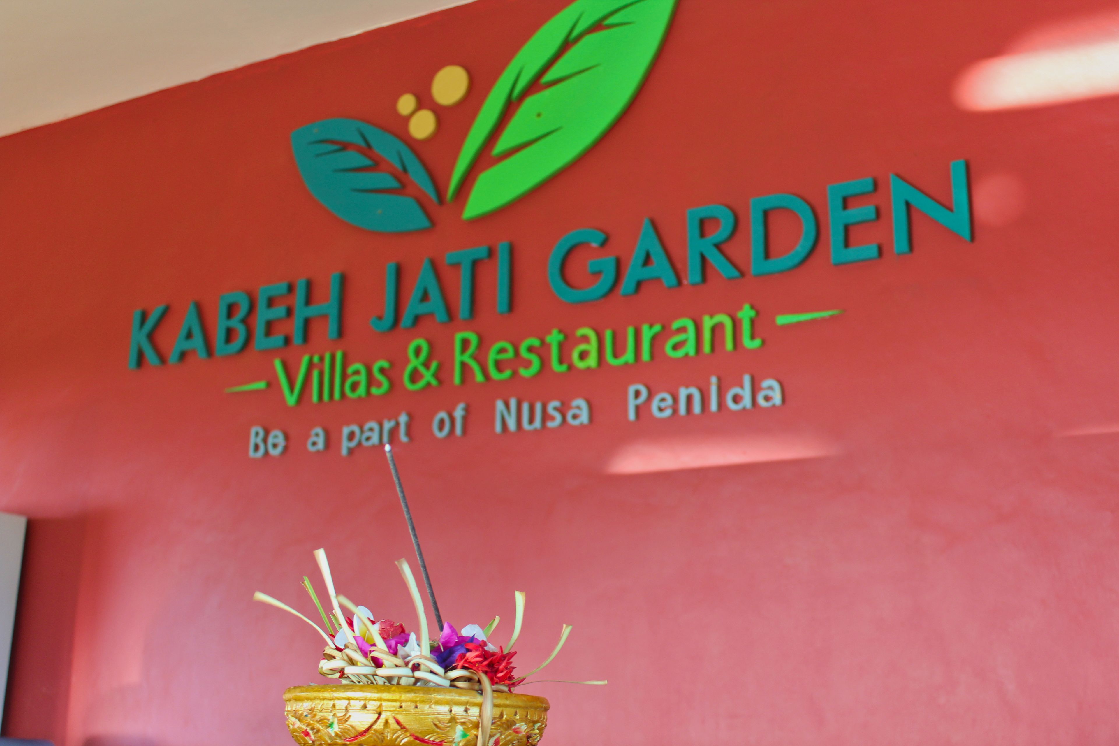A sign for Kabeh Jati Garden Villas & Restaurant with a decorative plant in the foreground.