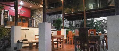 A restaurant with a stone wall, wooden furniture, and a red sign.