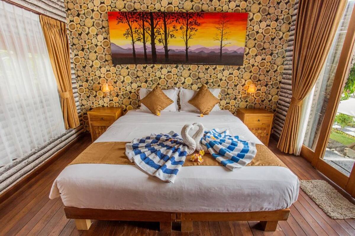 Un lit avec une serviette à carreaux, des oreillers et un tableau représentant des arbres accroché au mur.