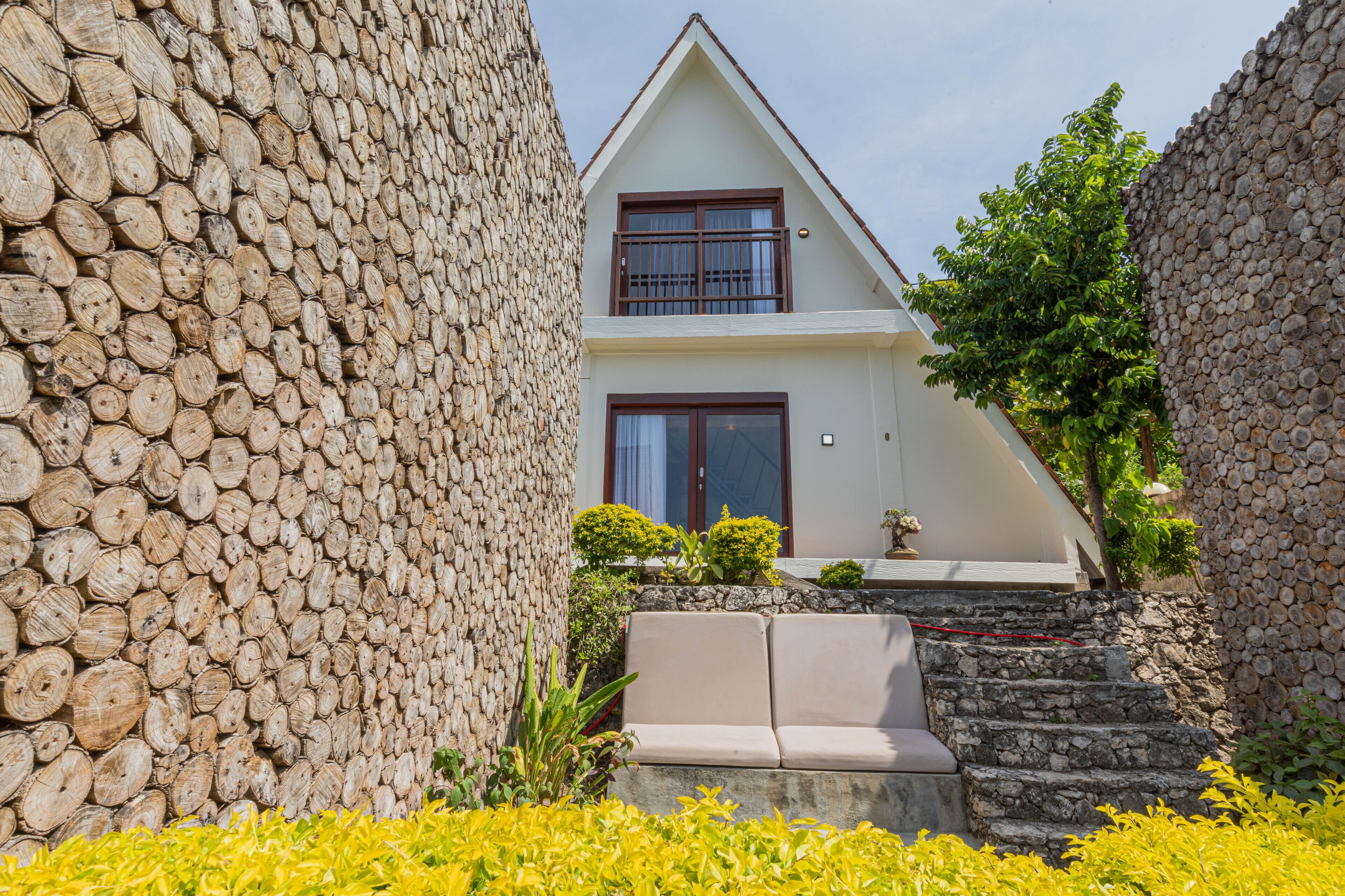A house with a stone wall, a white exterior, and a beige couch in front.