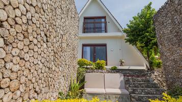 A house with a stone wall, a white exterior, and a beige couch in front.
